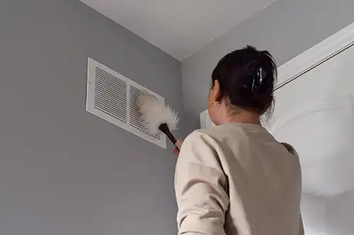 Sho-Me Clean Duct Cleaning - Woman using a duster to clean a vent in her home in Branson, MO.